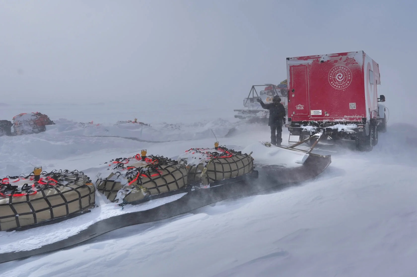 A truck hauls a loaded trailer uphill in the snow.